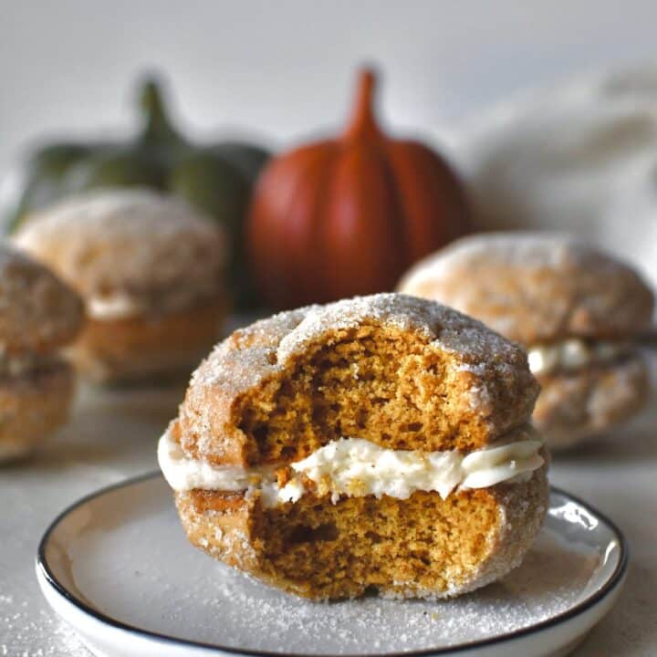 A Pumpkin Whoopie Pie on a plate with a bite taken out of it, surrounded by more whole pies.