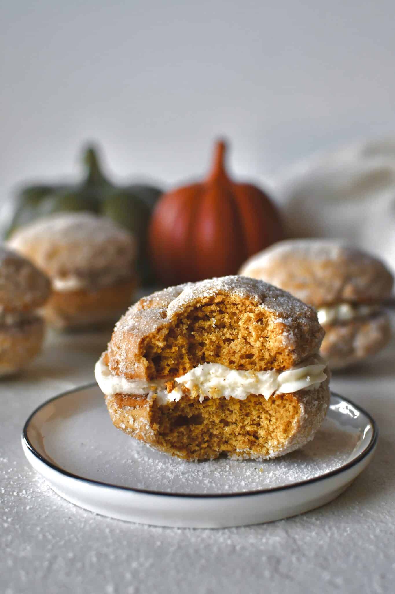 A Pumpkin Whoopie Pie on a plate with a bite taken out of it, surrounded by more whole pies.