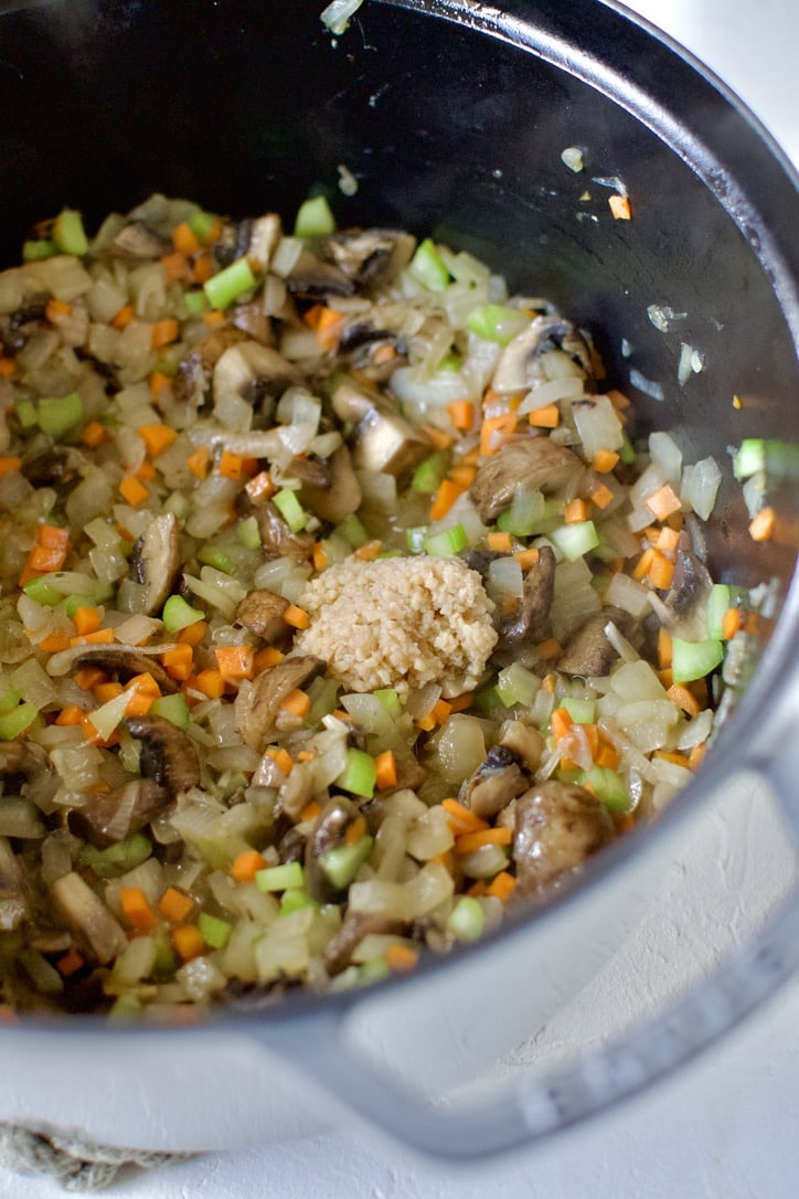 Cooked mushrooms, onions, celery, and carrots, in the bottom of a large pot, adding the garlic.