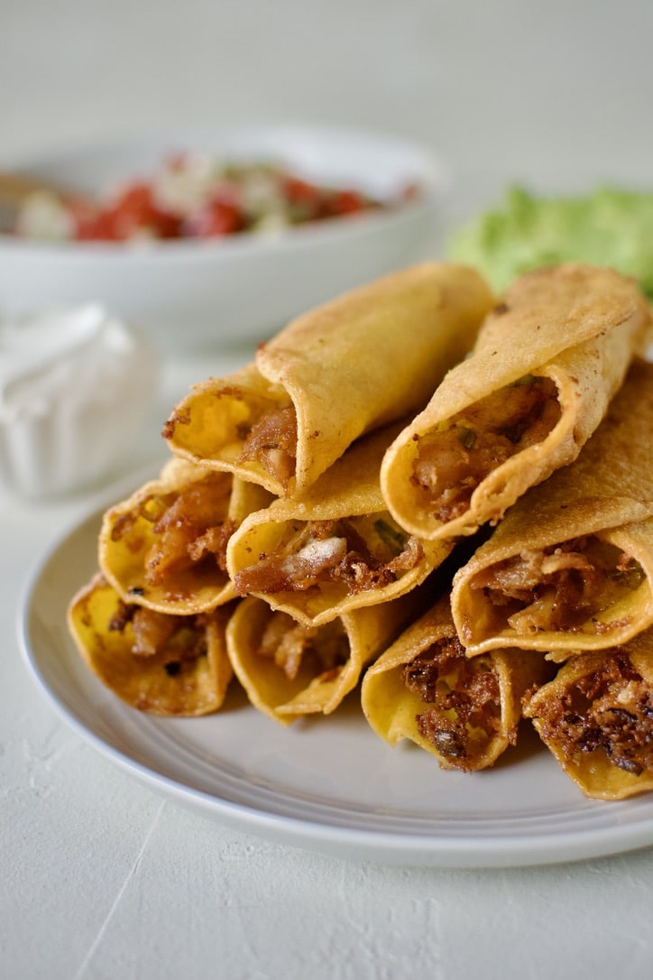 Cooked flautas stacked up on a plate cooling.