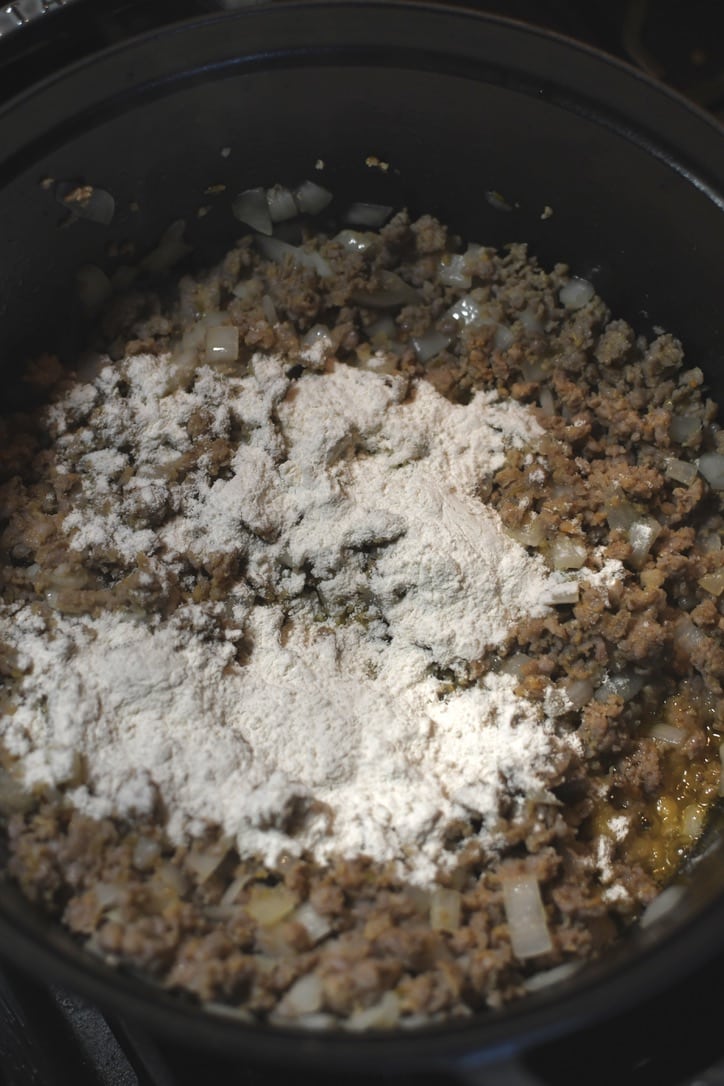 Placing the flour in the pot to form a roux in the fat of the sausage.