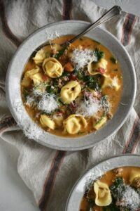 Creamy Sausage Tortellini Soup in a bowl with topped with finely shaved parmesan, ready to eat.