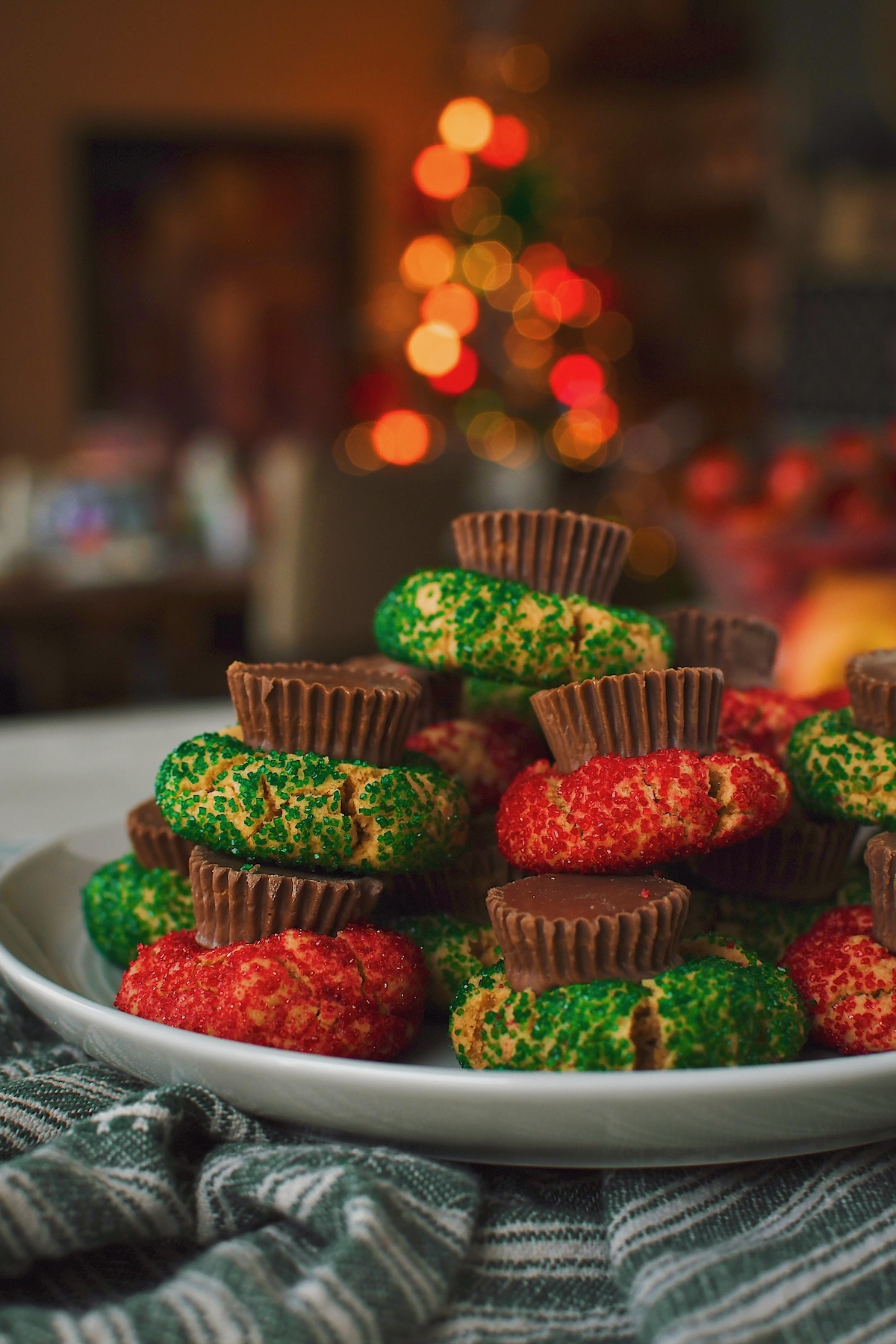 Stacked on a plate, an array of peanut butter cup cookies, with a lit christmas tree in the background, ready to be enjoyed.