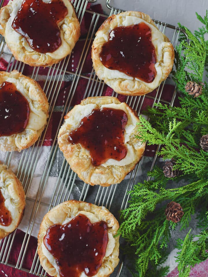 Sugar Plum Cheese Danish on a wire cooling rack over a Christmas themed towel and some greens on the side.