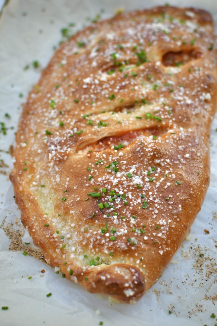 Calzone fresh out of the oven, brushed with garlic butter, and dusted with grated parmesan and chives.