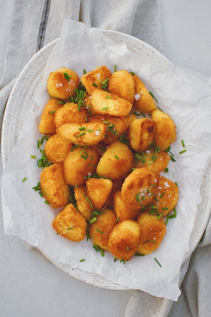 Crispy Roasted Potatoes on a platter topped with flakey sea salt and chopped chives.