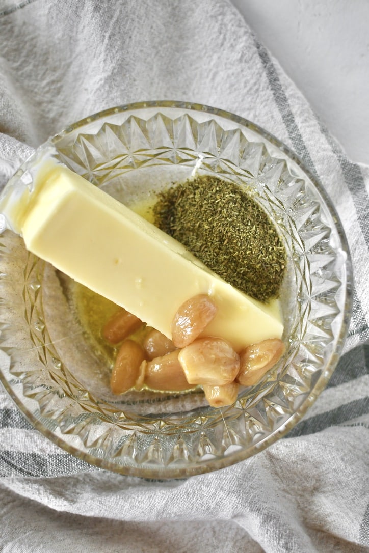 Butter, herbs de Provence, and confit garlic in a bowl, ready to be mixed together.