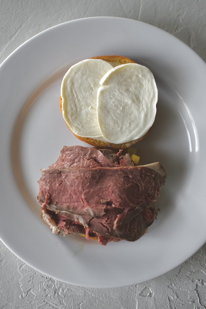 Assembling a roast beef sandwich; adding the carved roast beef to the other sandwich toppings.