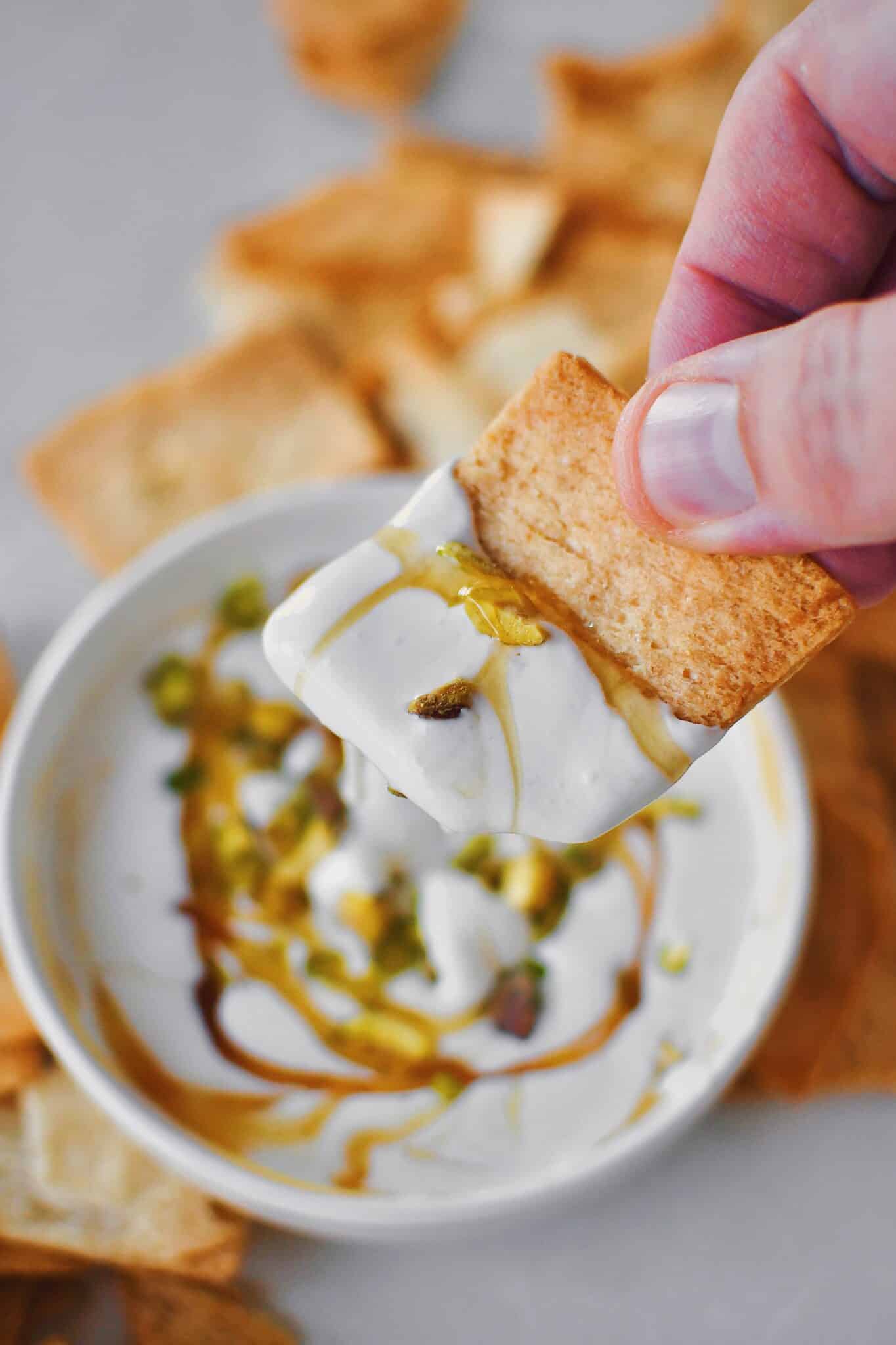 A pita chip in hand, that has been dipped in whipped feta dip that has been served with honey and pistachios.