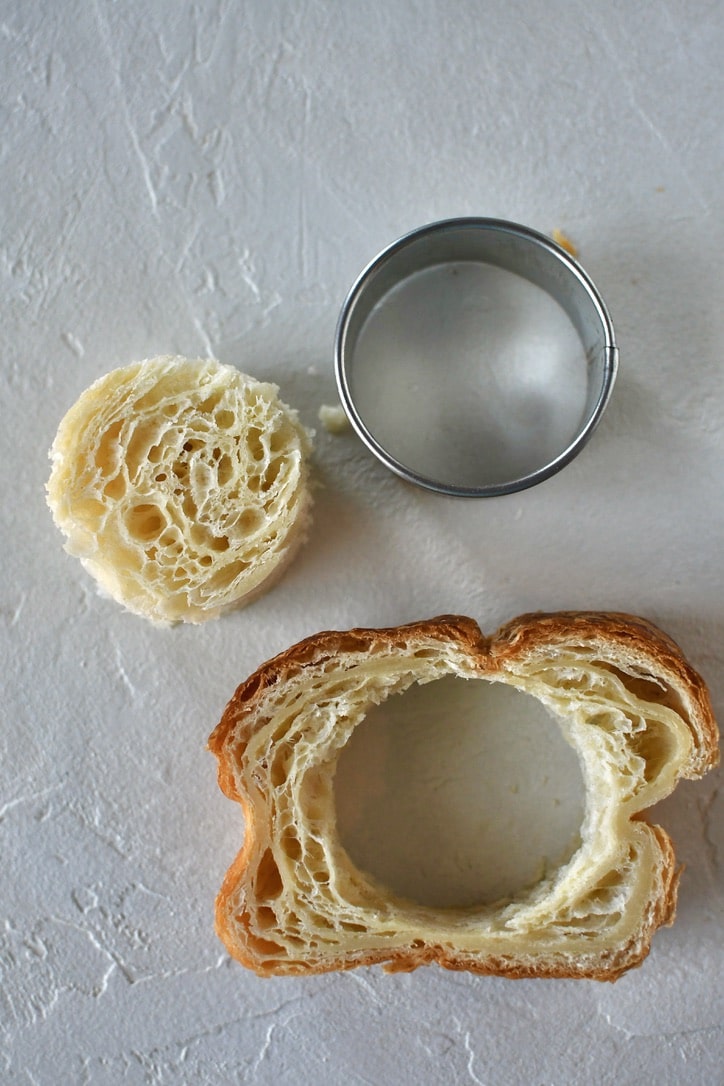 Croissant Toast on a work surface with a round cutter next to it and the center cut out of the bread.