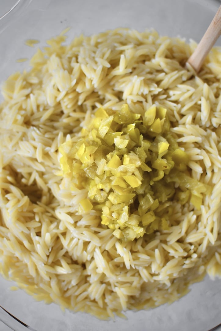 Adding the cooked and cooled orzo to the bowl of veggies with the pepperoncini peppers.