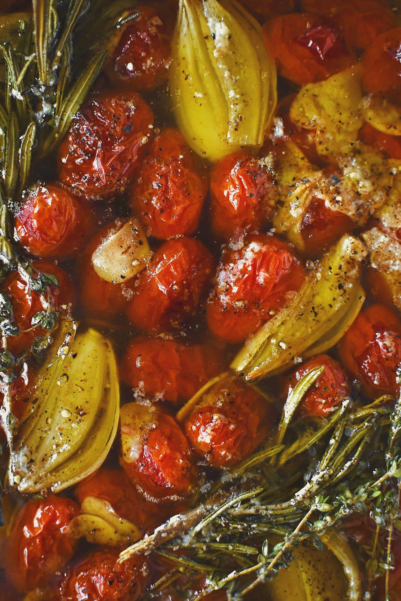 Grape tomatoes in a pan with shallots, sliced garlic, thyme, rosemary, salt, and pepper after roasting and made into confit.