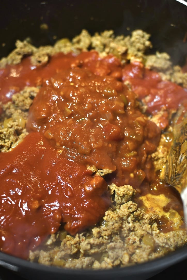 Adding the tomato sauce and salsa to the browned and seasoned turkey and onions, before simmering.