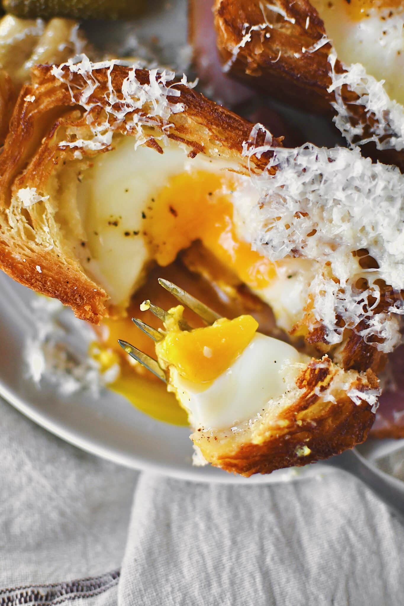 Toad in a Hole served over a ham steak and topped with gruyere cheese, cut open and the yolk running out.