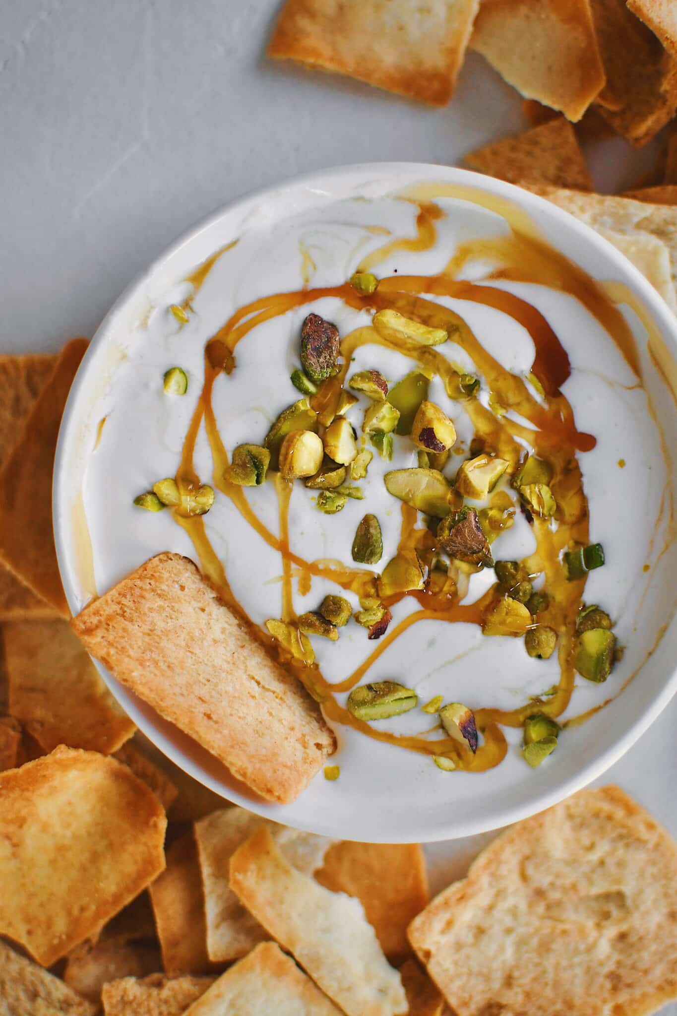 A pita chip dipped in whipped feta dip that has been served with honey and pistachios.