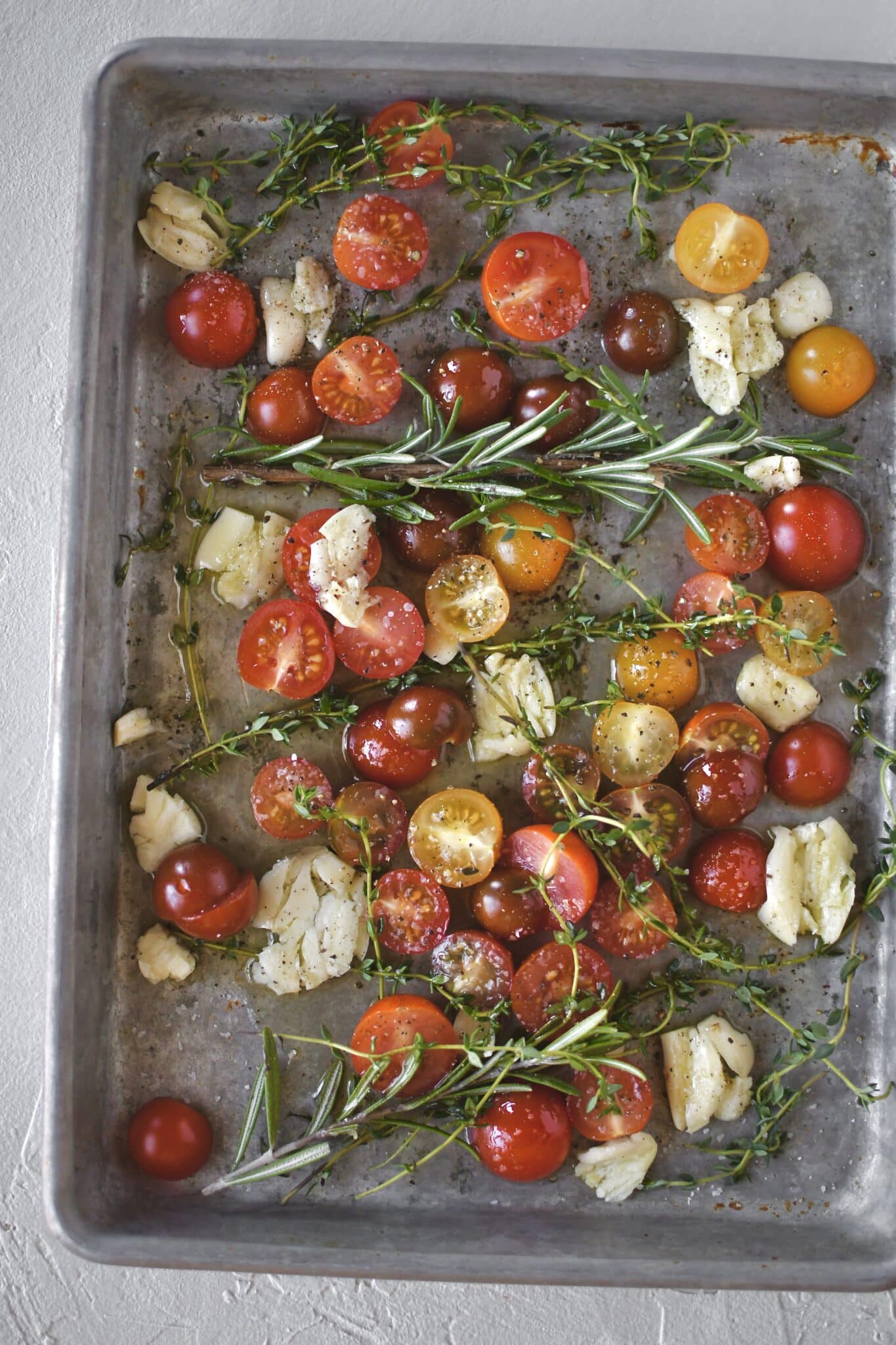 Seasoned cherry tomatoes, garlic, and herbs, before roasting.