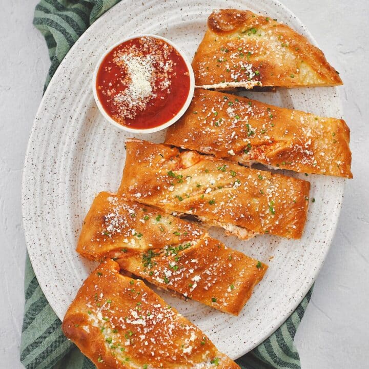 Calzone fresh out of the oven, brushed with garlic butter, and dusted with grated parmesan and chives and sliced. Served with a side of marinara sauce.