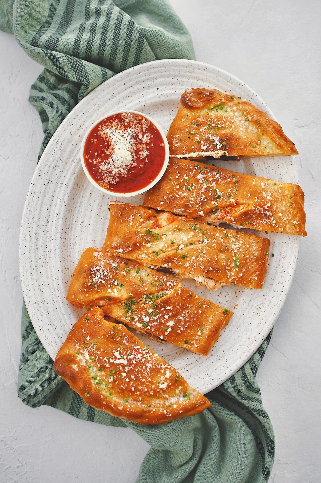 Calzone fresh out of the oven, brushed with garlic butter, and dusted with grated parmesan and chives and sliced. Served with a side of marinara sauce.