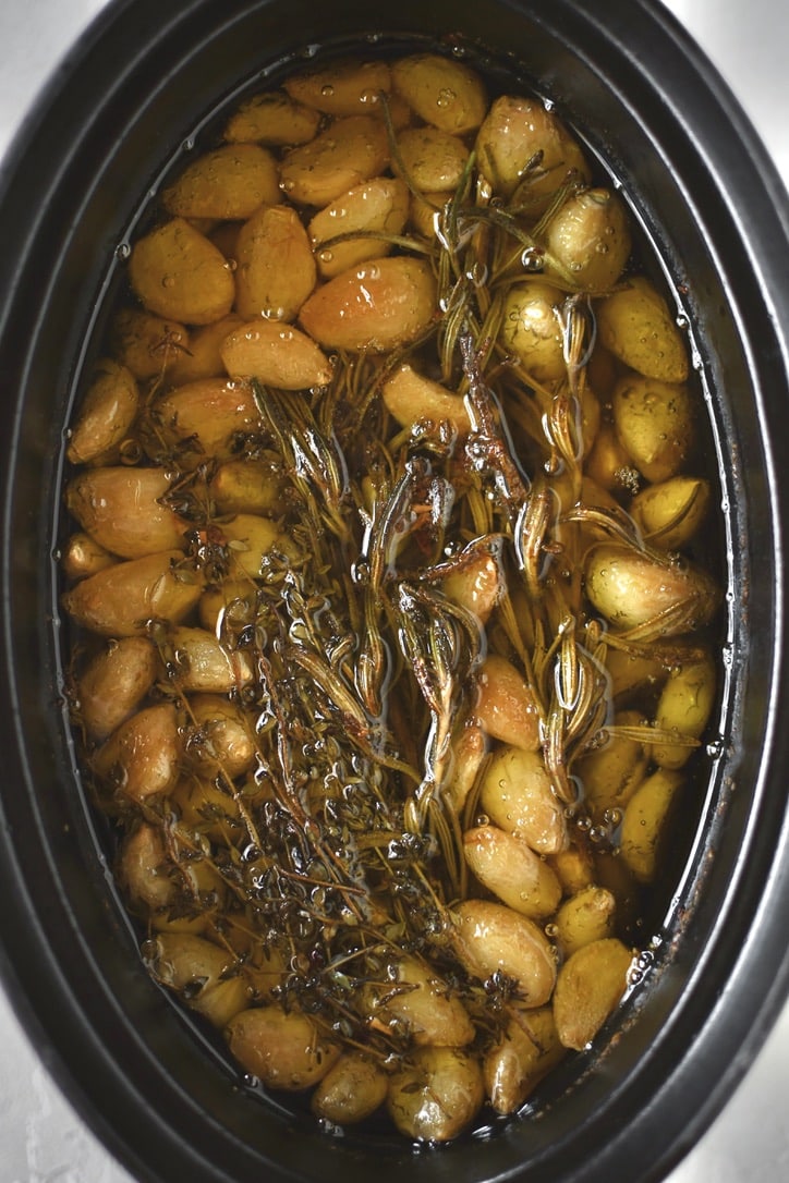 Garlic cloves in a cast iron pot after adding the herbs and olive oil. After cooking.