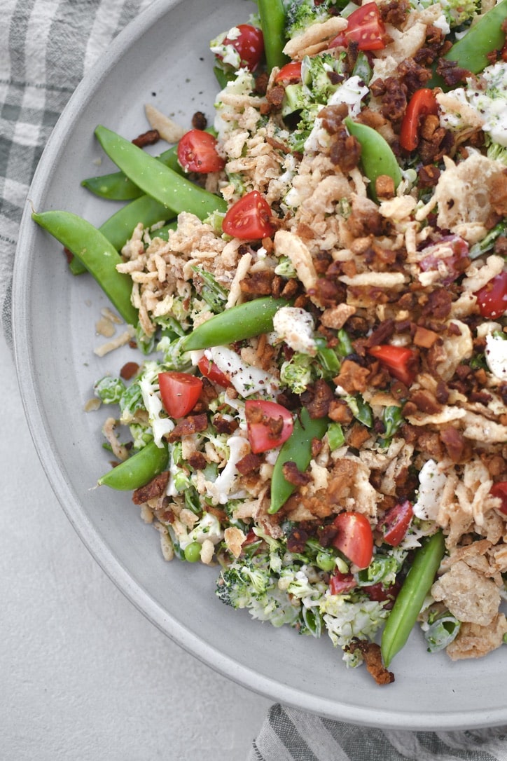 Snap Pea Salad on a platter topped with bacon bits and crispy onions ready to eat.