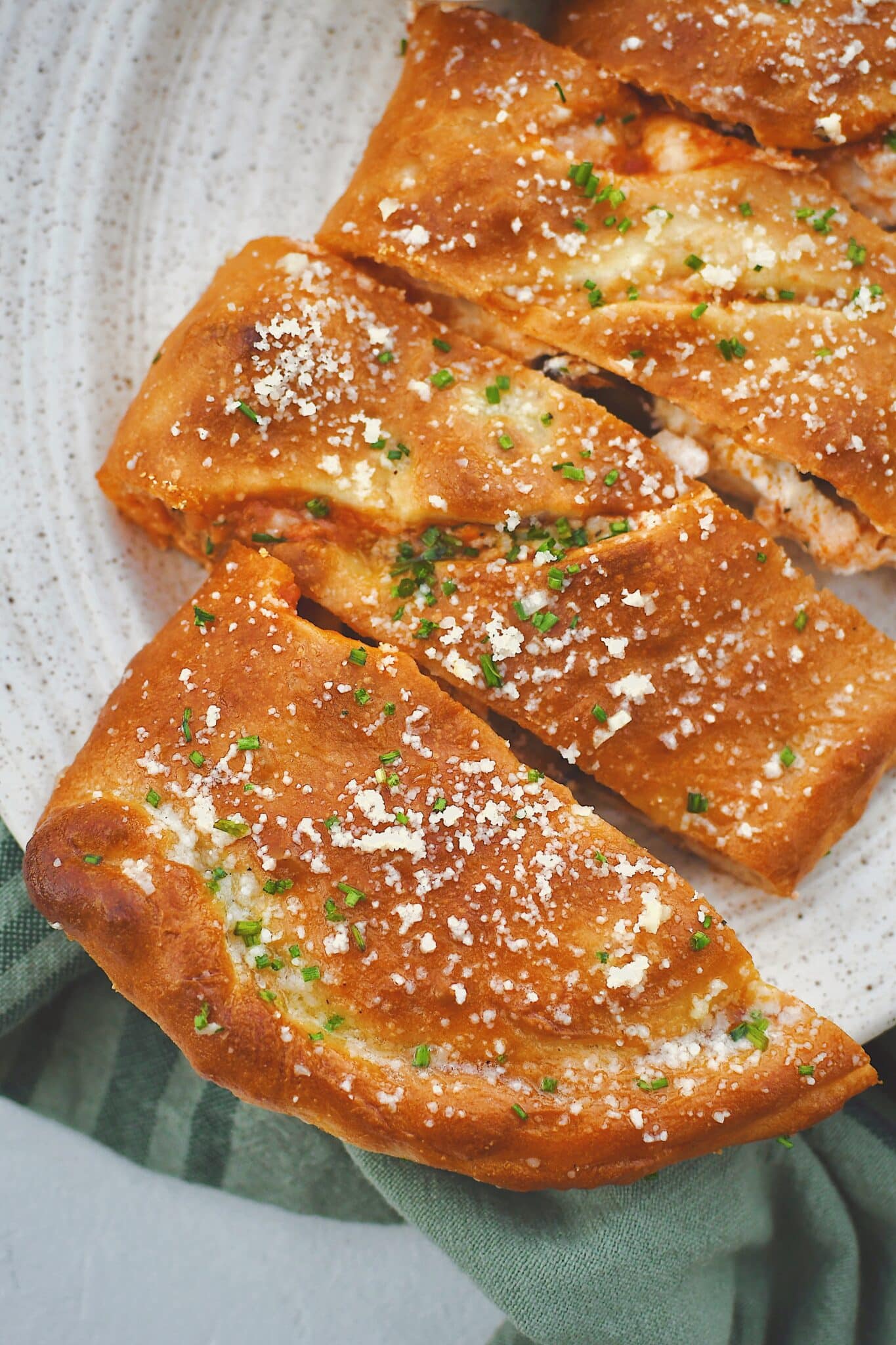 Calzone fresh out of the oven, brushed with garlic butter, and dusted with grated parmesan and chives and sliced. Served with a side of marinara sauce.