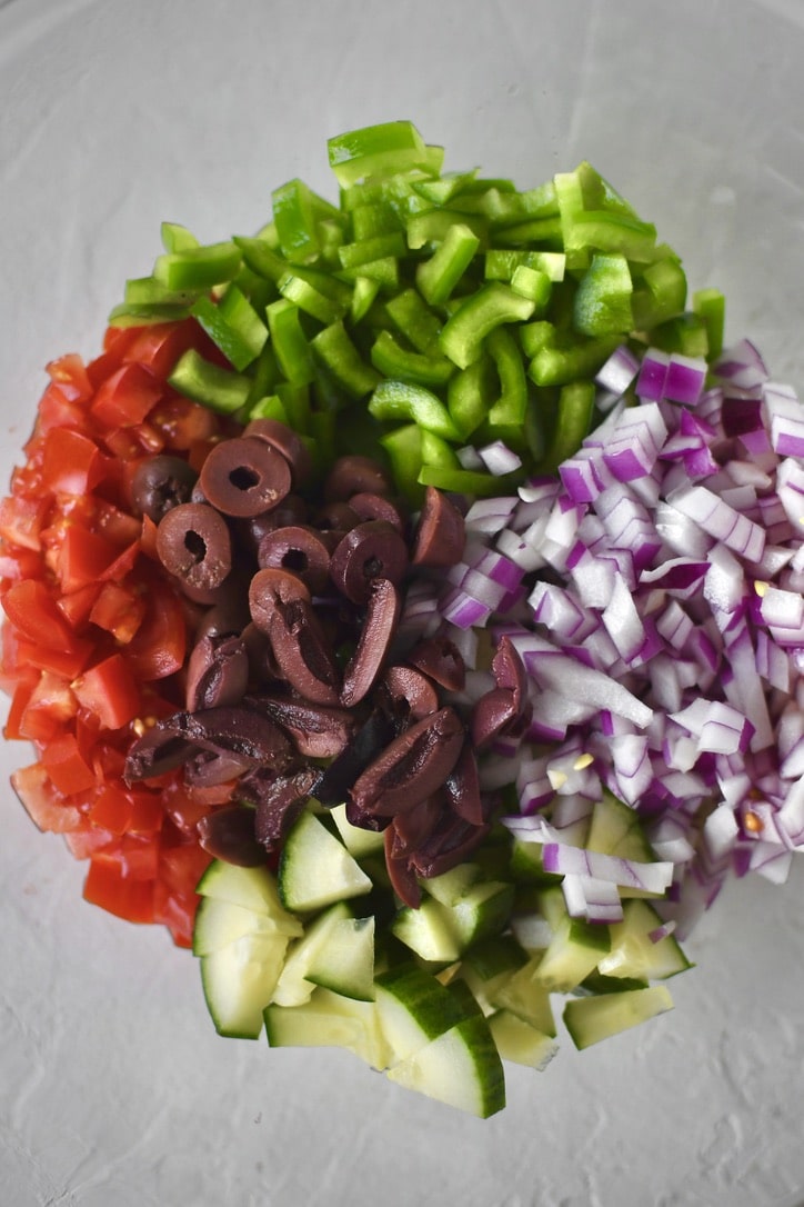 Adding the chopped vegetables and olives to a bowl.