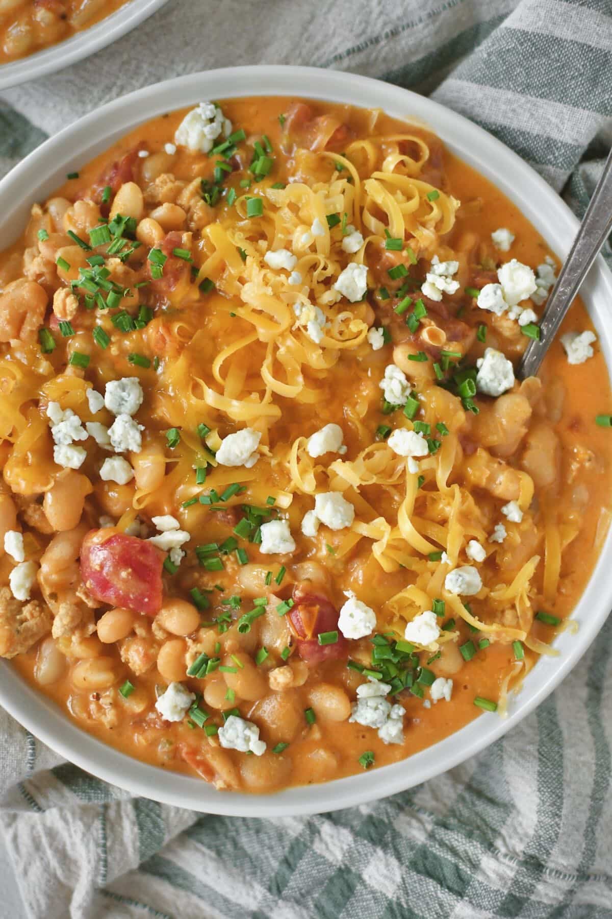 Buffalo Chicken Chili served in a bowl, topped with chives, blue cheese, and cheddar cheese.