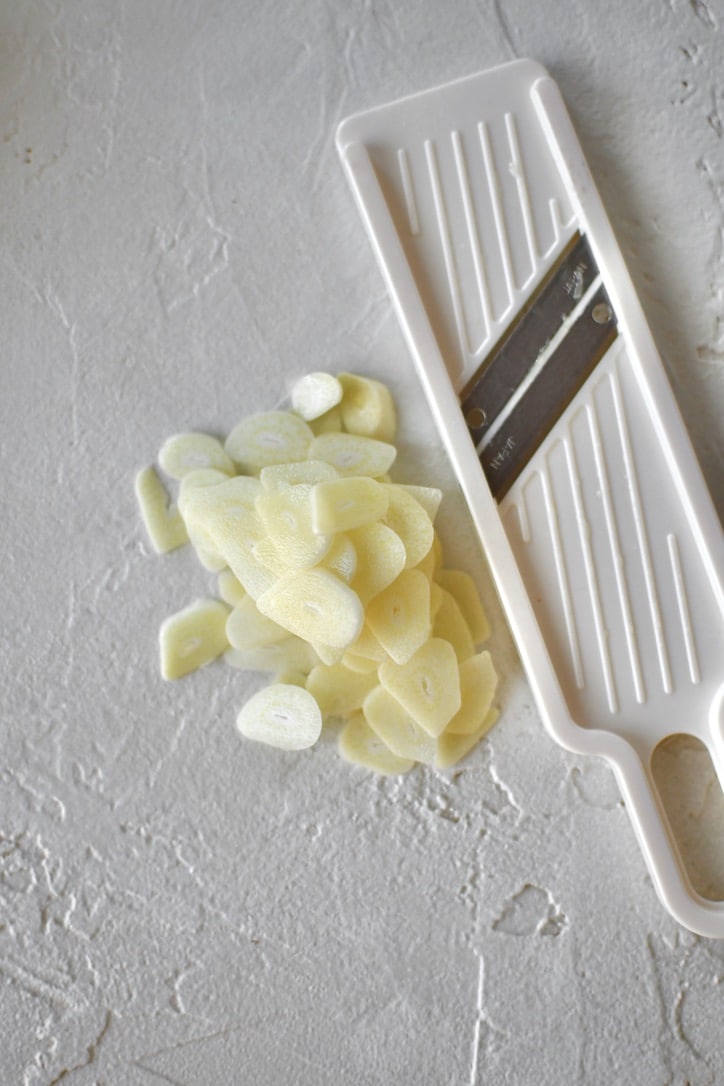 Sliced garlic that has been sliced on a mini mandoline that is sitting next to it.