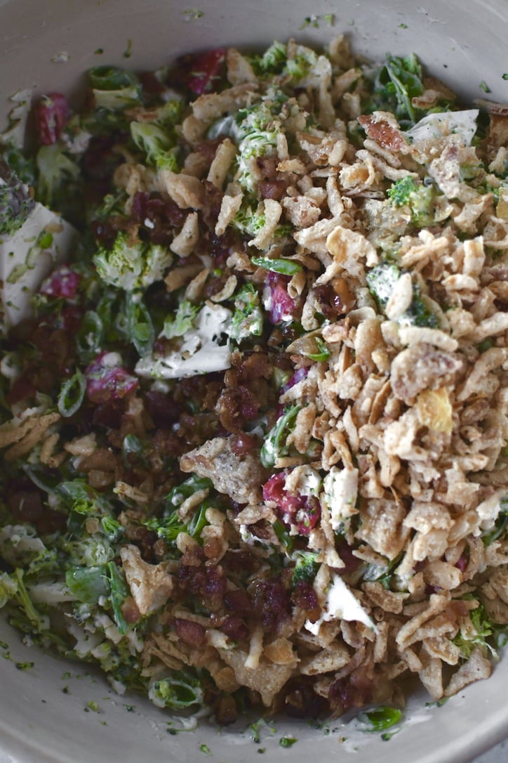 peas, broccoli, cauliflower, and tomatoes cut up and tossed with dressing. adding bacon and crispy onions to the bowl.