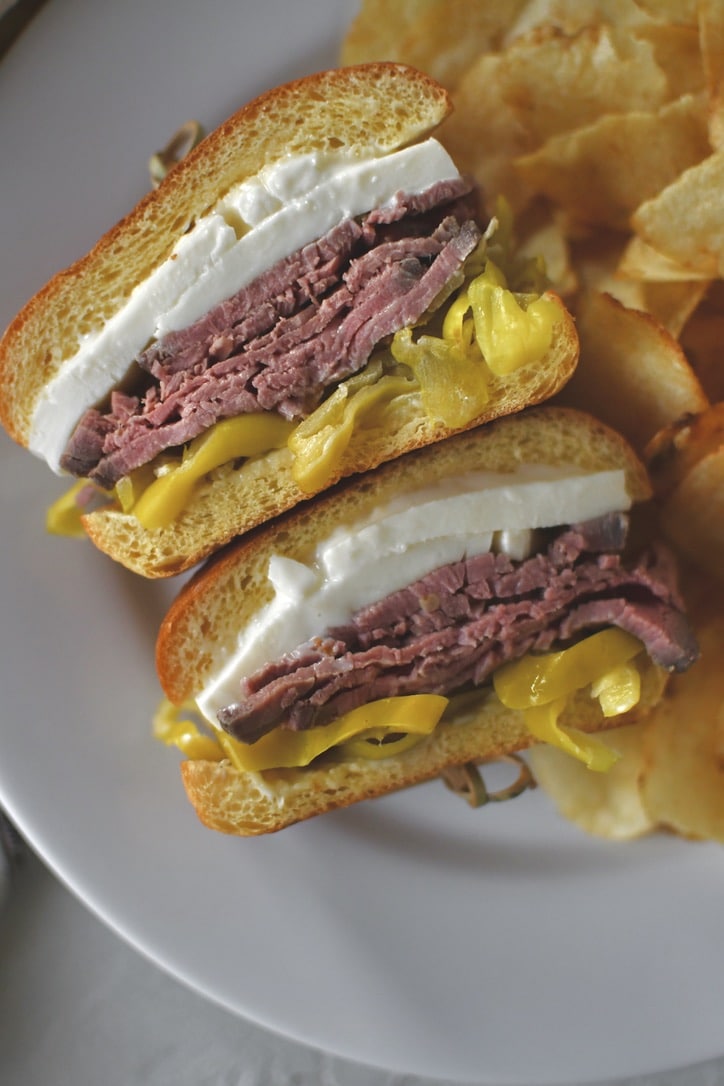 Fully assembled roast beef sandwich, cut in half and on a plate with some chips ready to eat.