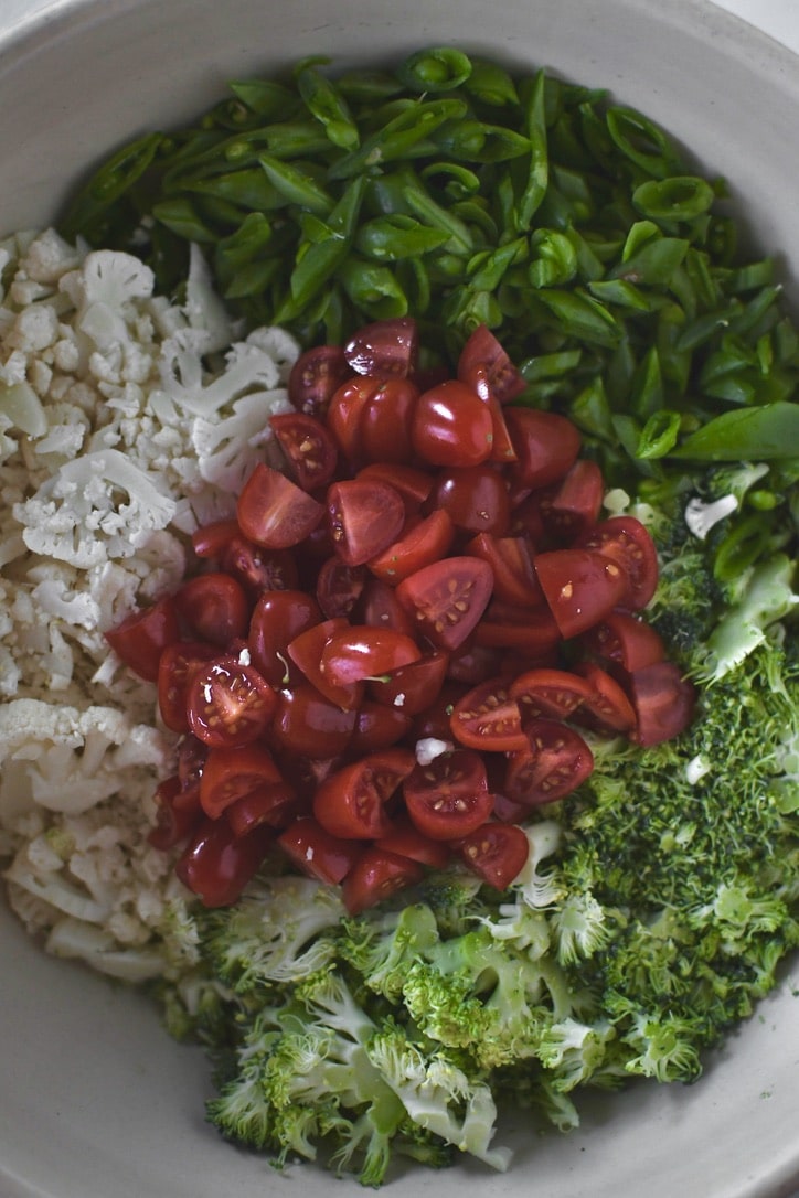 peas, broccoli, cauliflower, and tomatoes cut up ready to be tossed with dressing.