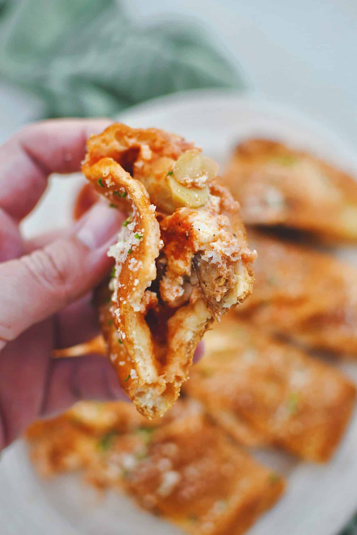 Holding a piece of calzone in hand with a bite taken out of it, showing all the fillings inside.