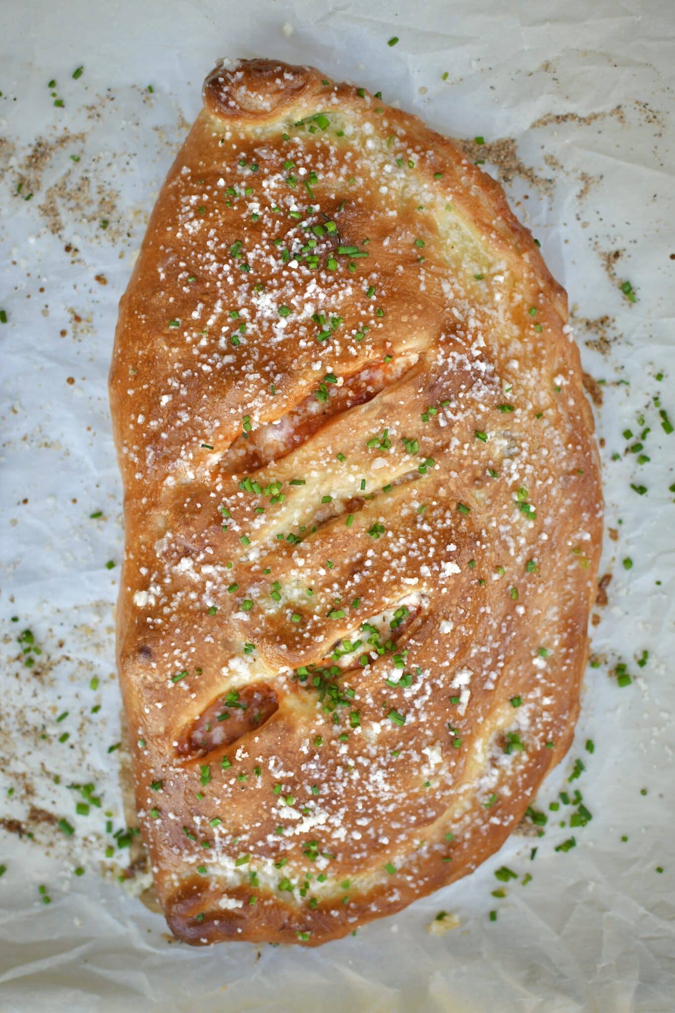 Calzone fresh out of the oven, brushed with garlic butter, and dusted with grated parmesan and chives.