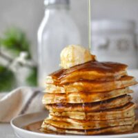 Eggnog Pancakes with maple syrup being drizzled over a stack of them.