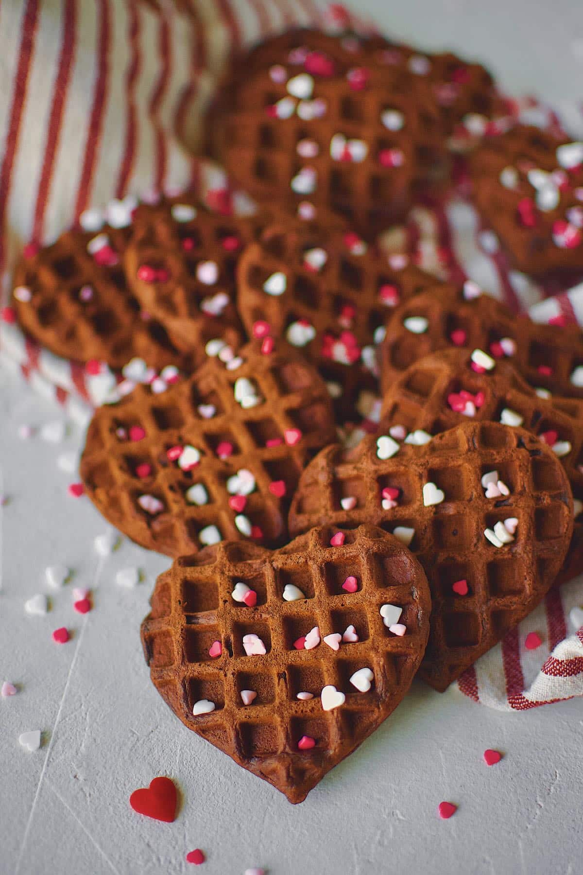 Red Velvet Waffles in the shape of hearts on a tray topped heart sprinkles.