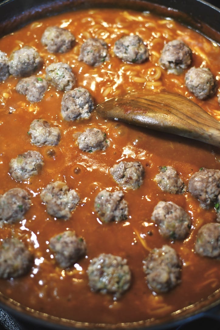 Gently placing the cooked meatballs in the pan.