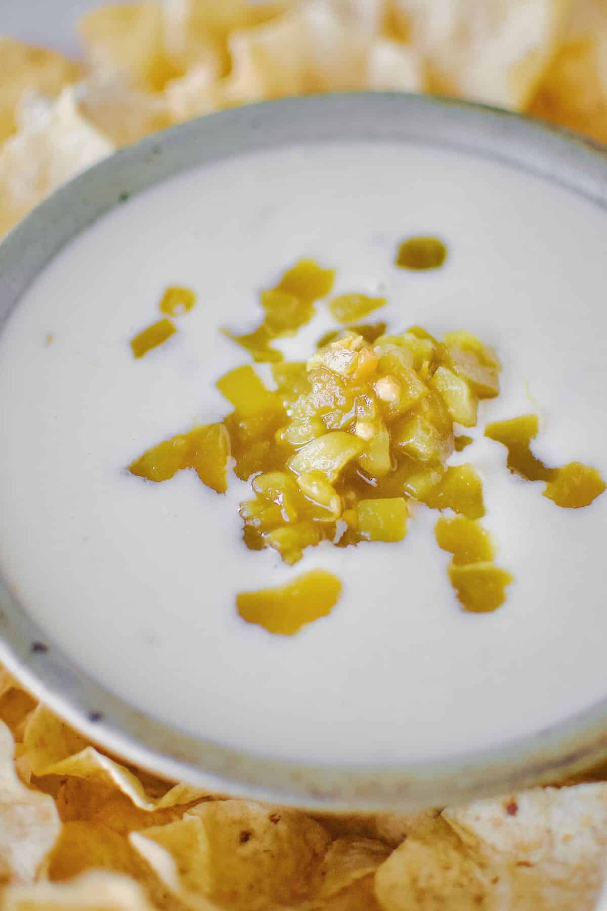 White Queso Dip in a bowl, surrounded by chips, topped with green chilis.