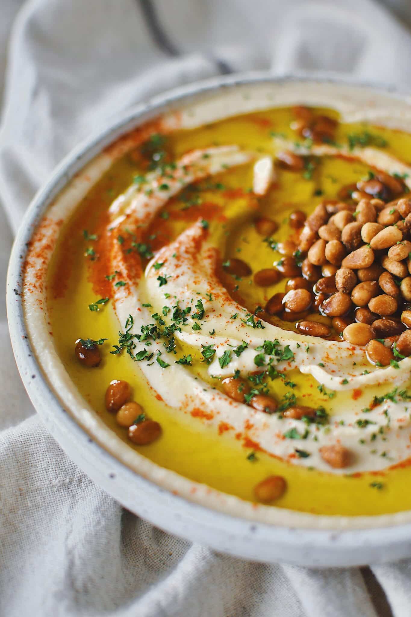 Homemade Hummus, topped with olive oil, paprika, toasted pine nuts, and parsley, ready to eat.