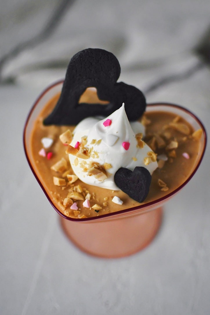Peanut Butter Mousse in a small heart shaped cup, topped with whipped cream, peanuts, and a chocolate wafer.