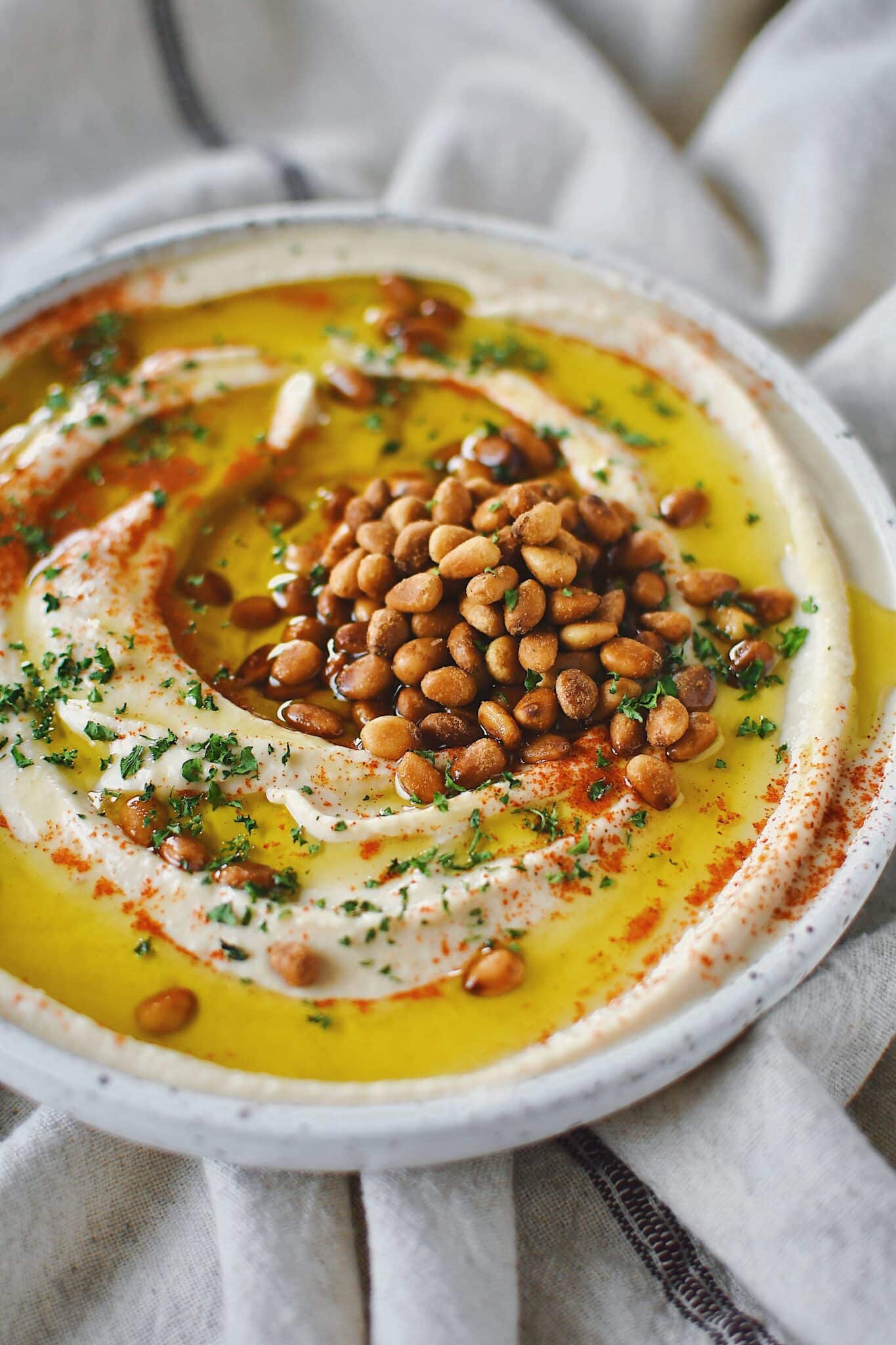 Homemade Hummus, topped with olive oil, paprika, toasted pine nuts, and parsley, ready to eat.