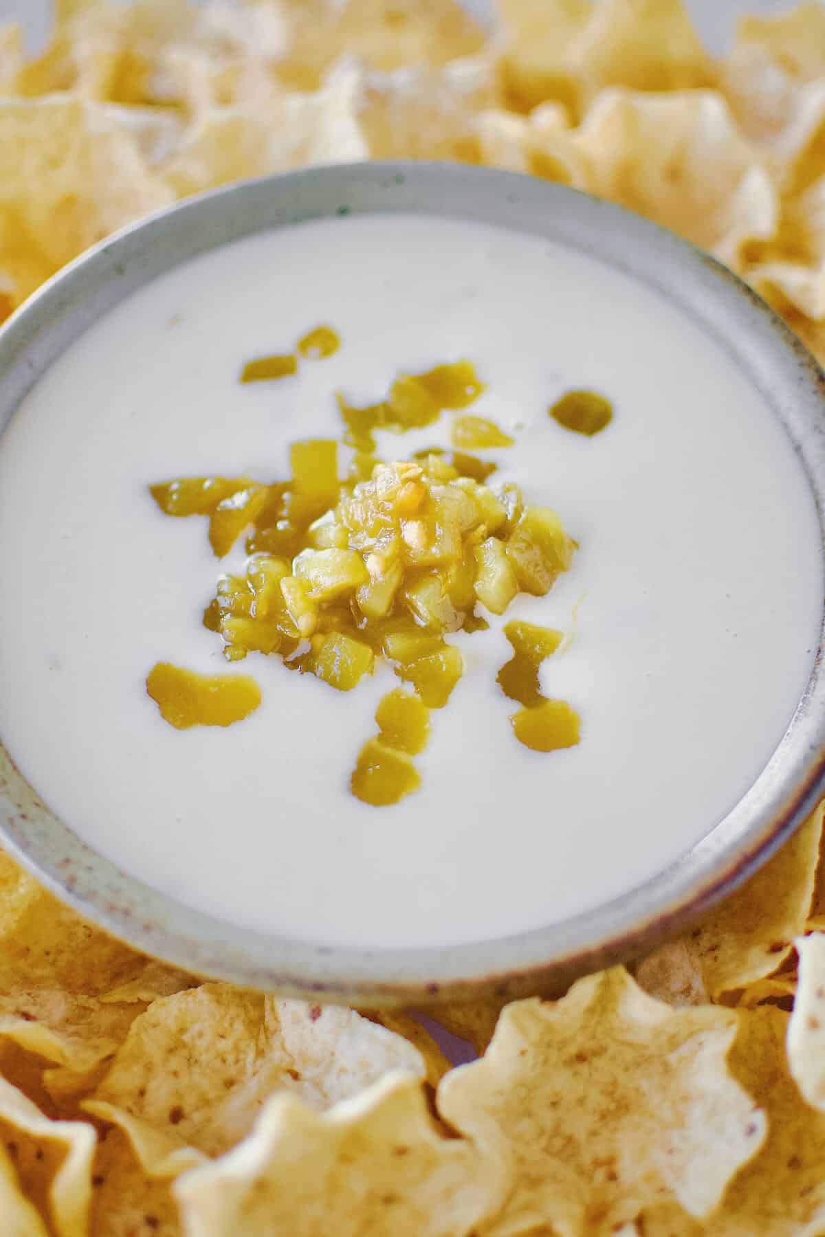 White Queso Dip in a bowl, surrounded by chips, topped with green chilis.