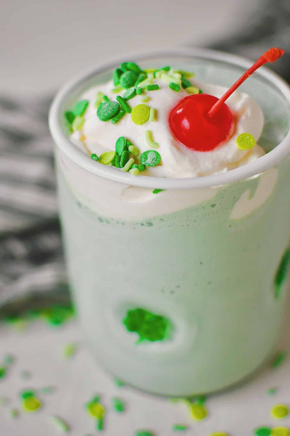 Shamrock Shake in a shamrock glass topped with whipped cream, sprinkles, and a cherry.