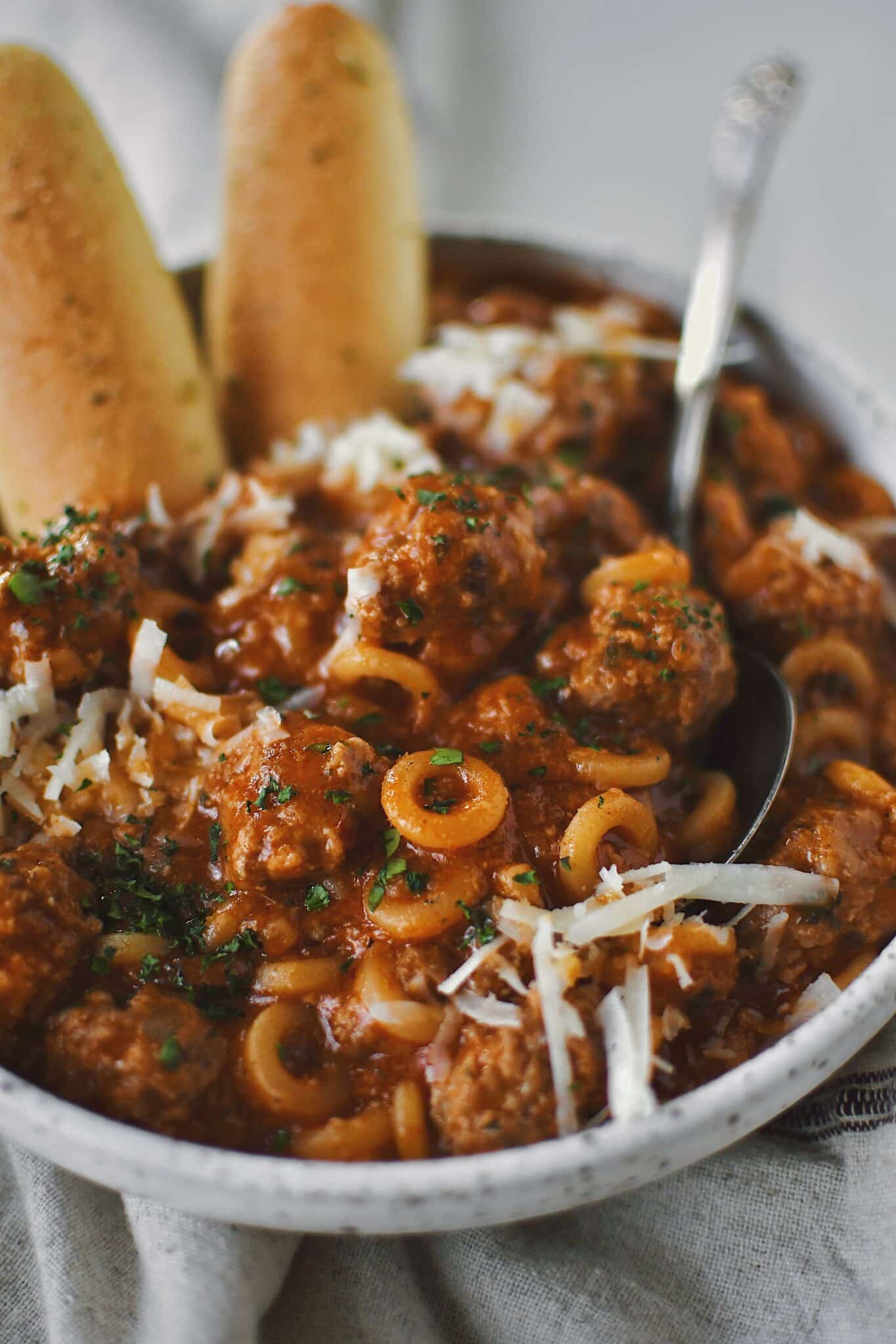 Homemade Spaghettios with meatballs in a bowl with a spoon topped with extra cheese and parsley.