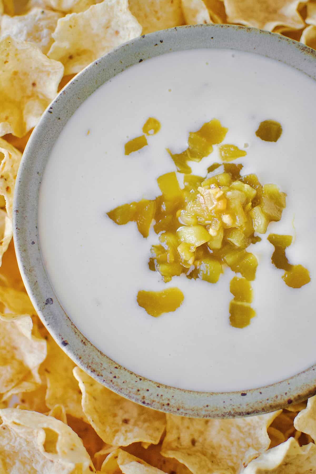 White Queso Dip in a bowl, surrounded by chips, topped with green chilis.