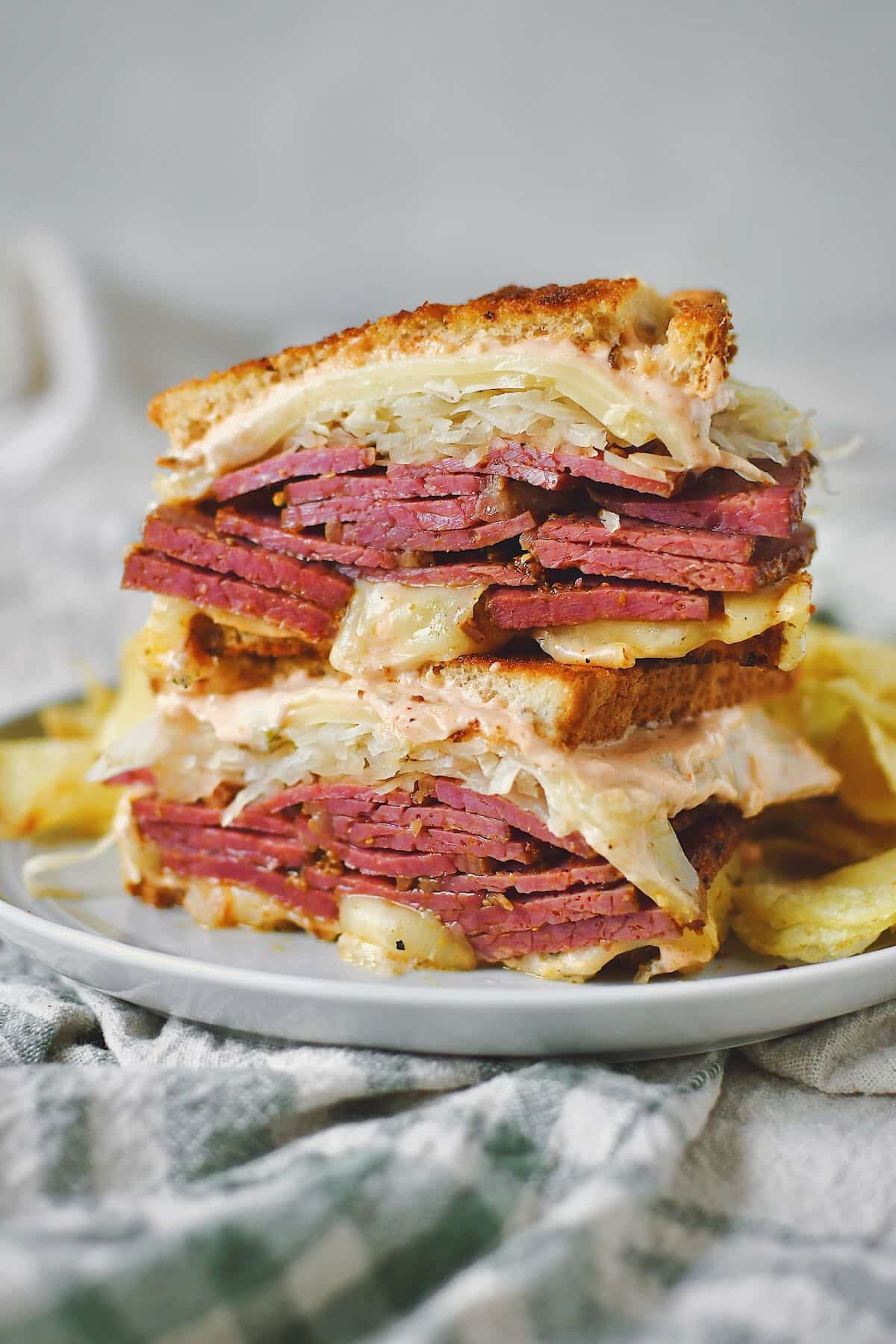 Finished Reuben Sandwich cut in half, on a plate, served with chips.