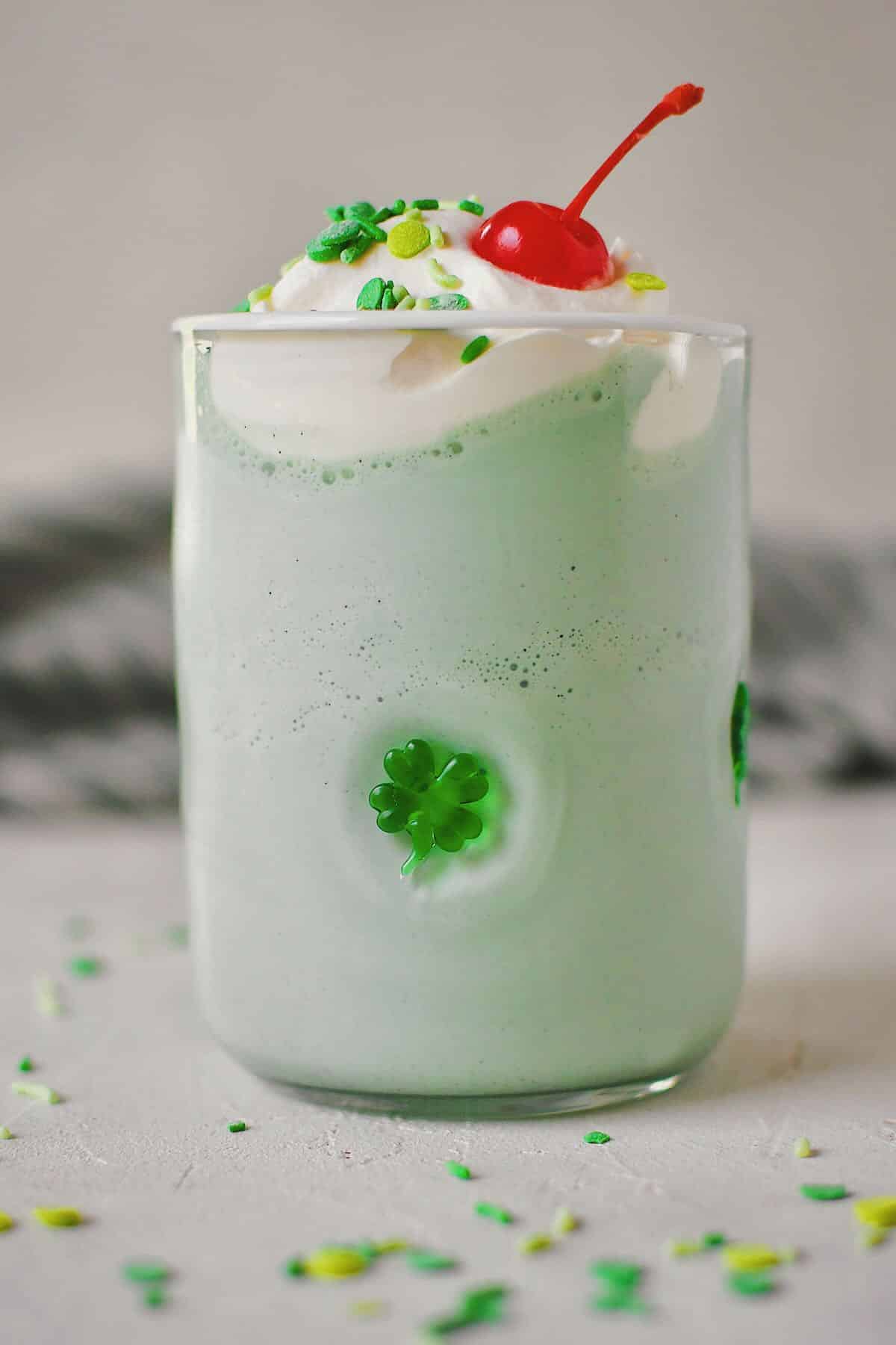 Shamrock Shake in a shamrock glass topped with whipped cream, sprinkles, and a cherry.
