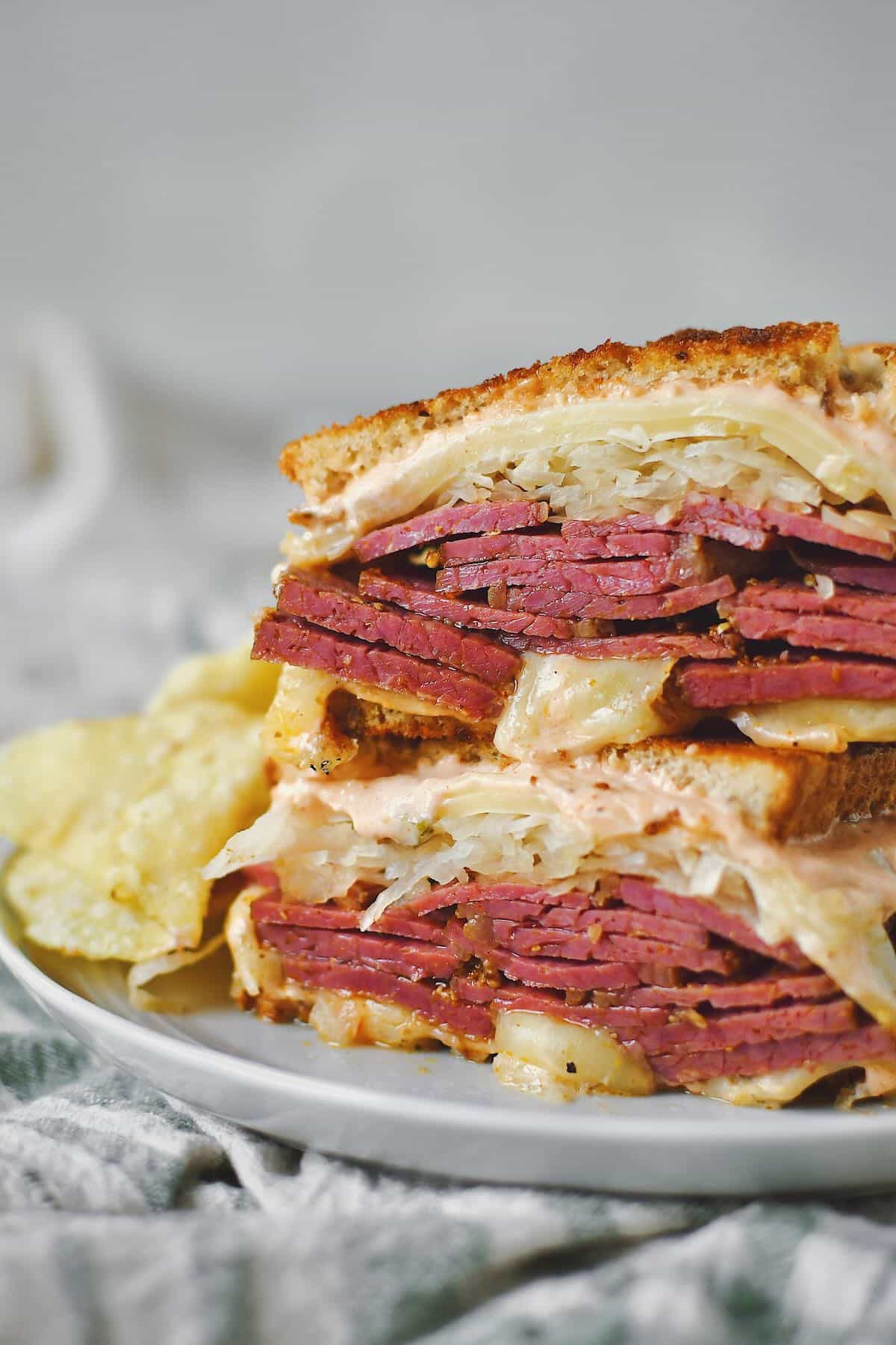 Finished Reuben Sandwich cut in half, on a plate, served with chips.