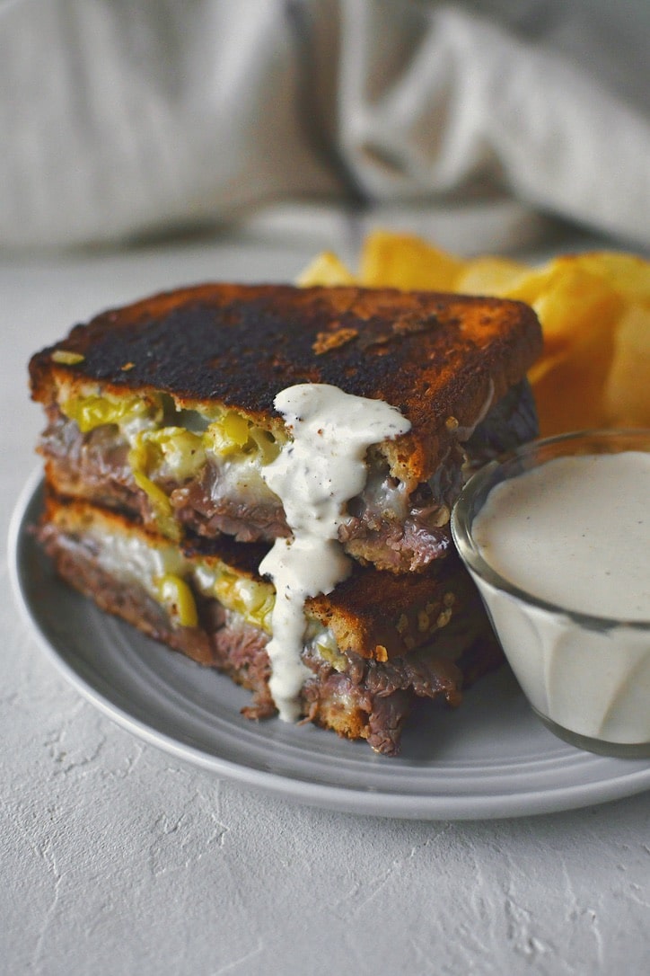A roast beef grilled cheese sandwich that has been dipped in horseradish cream sauce.
