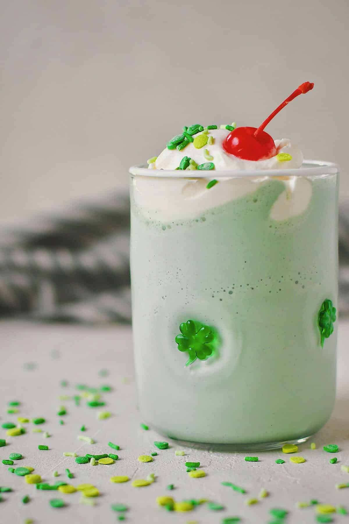 Shamrock Shake in a shamrock glass topped with whipped cream, sprinkles, and a cherry.