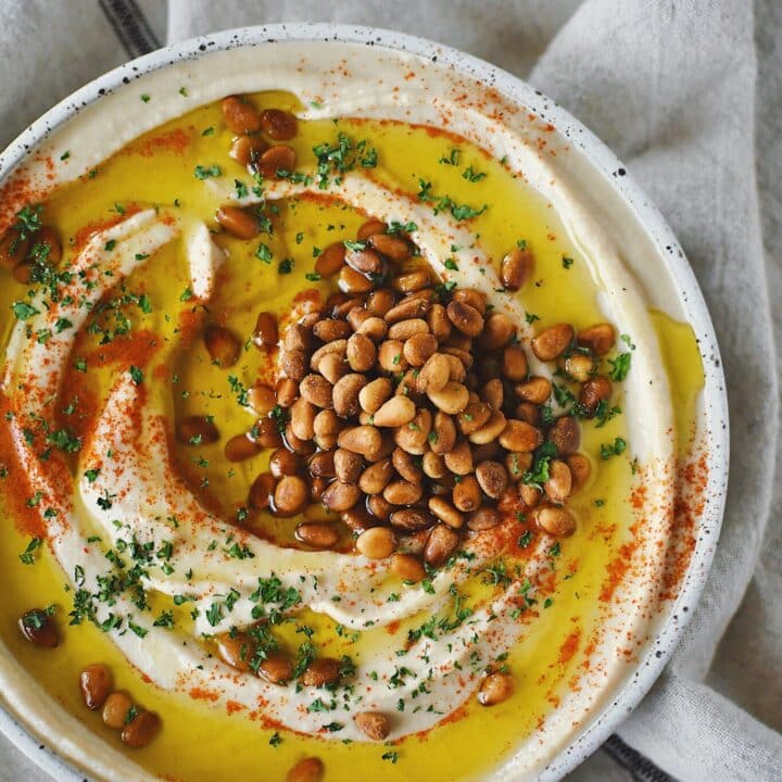 Homemade Hummus, topped with olive oil, paprika, toasted pine nuts, and parsley, ready to eat.